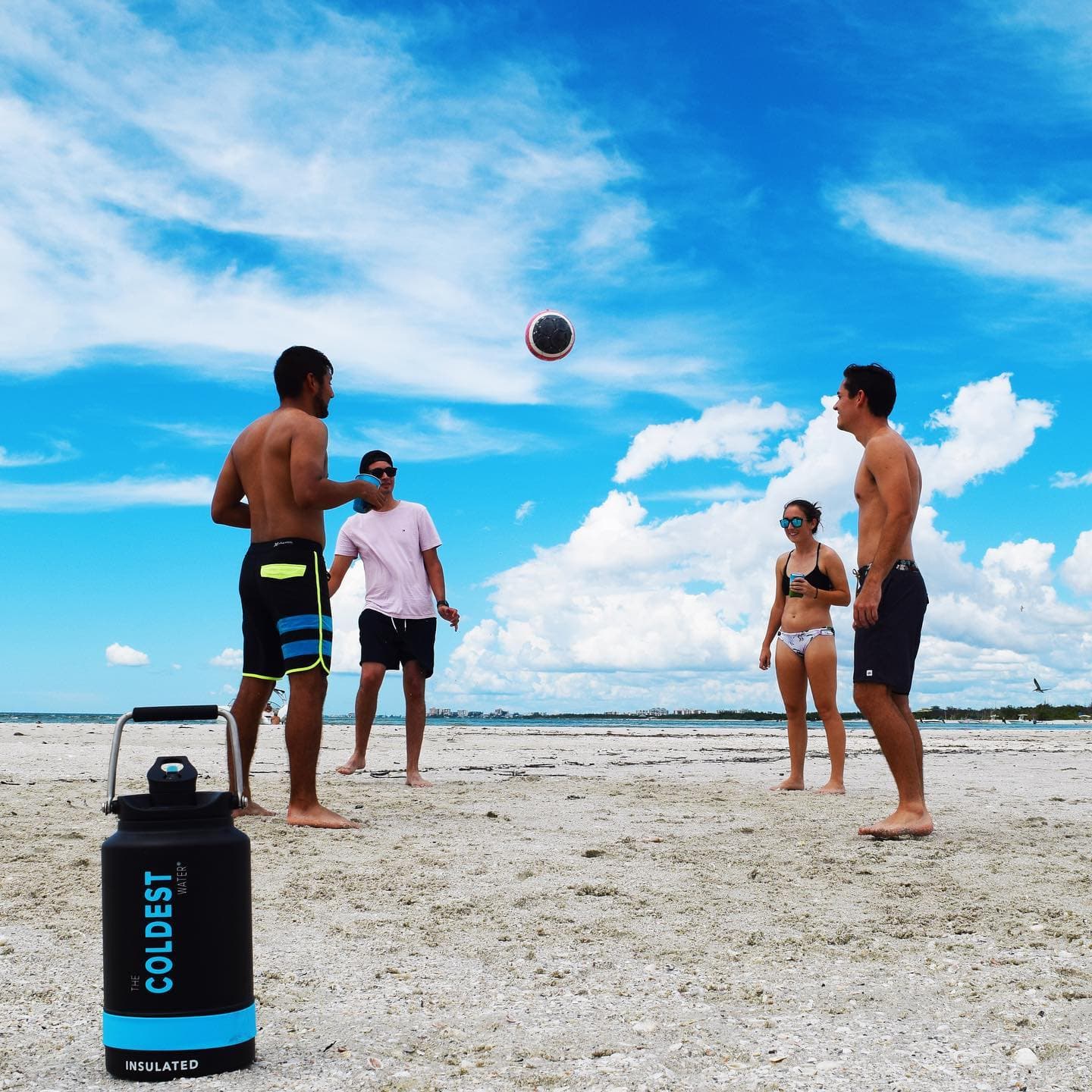 Group playing beach volleyball with a Coldest bottle nearby